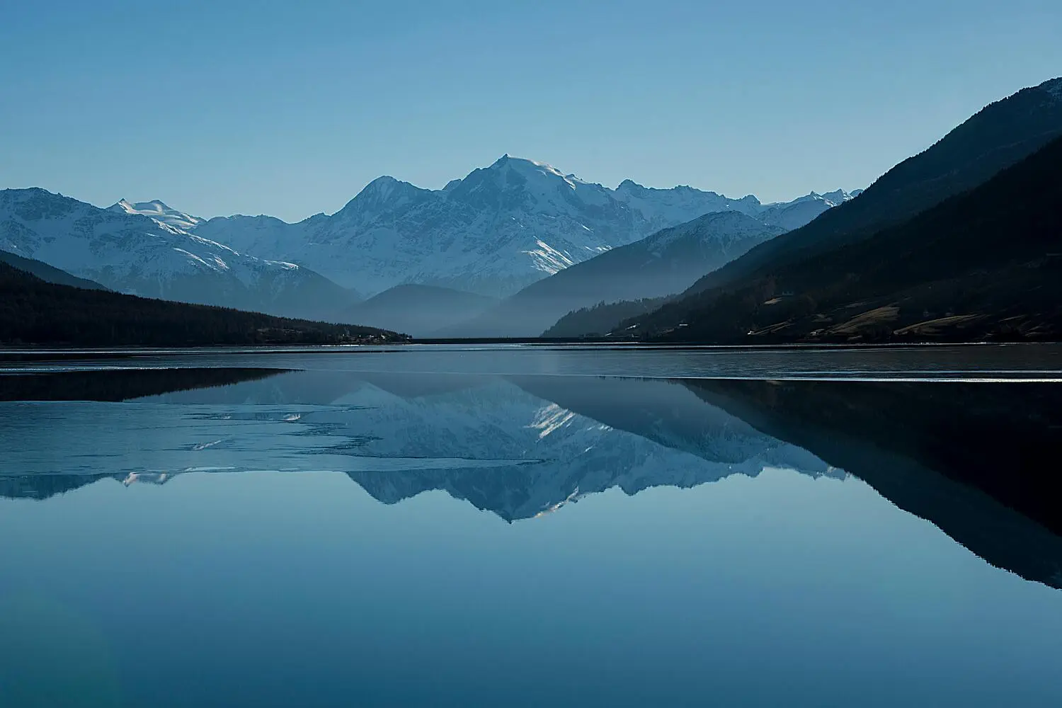 Un paysage de montagne avec des sommets enneigés reflétés de manière presque parfaite dans un lac calme.